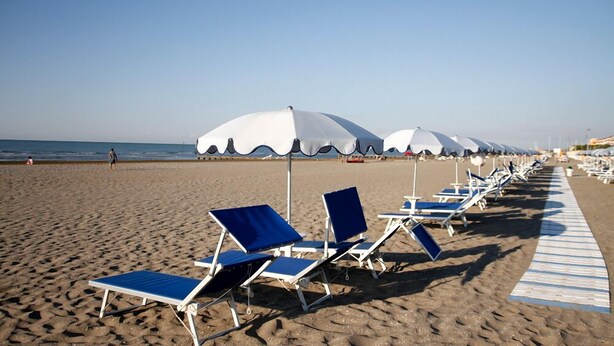 Une plage bordée de rangées de chaises longues bleues et de parasols blancs.