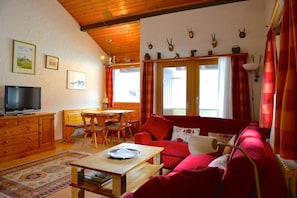 A cozy living room with a red sofa, wooden furniture, a television, and a dining area.