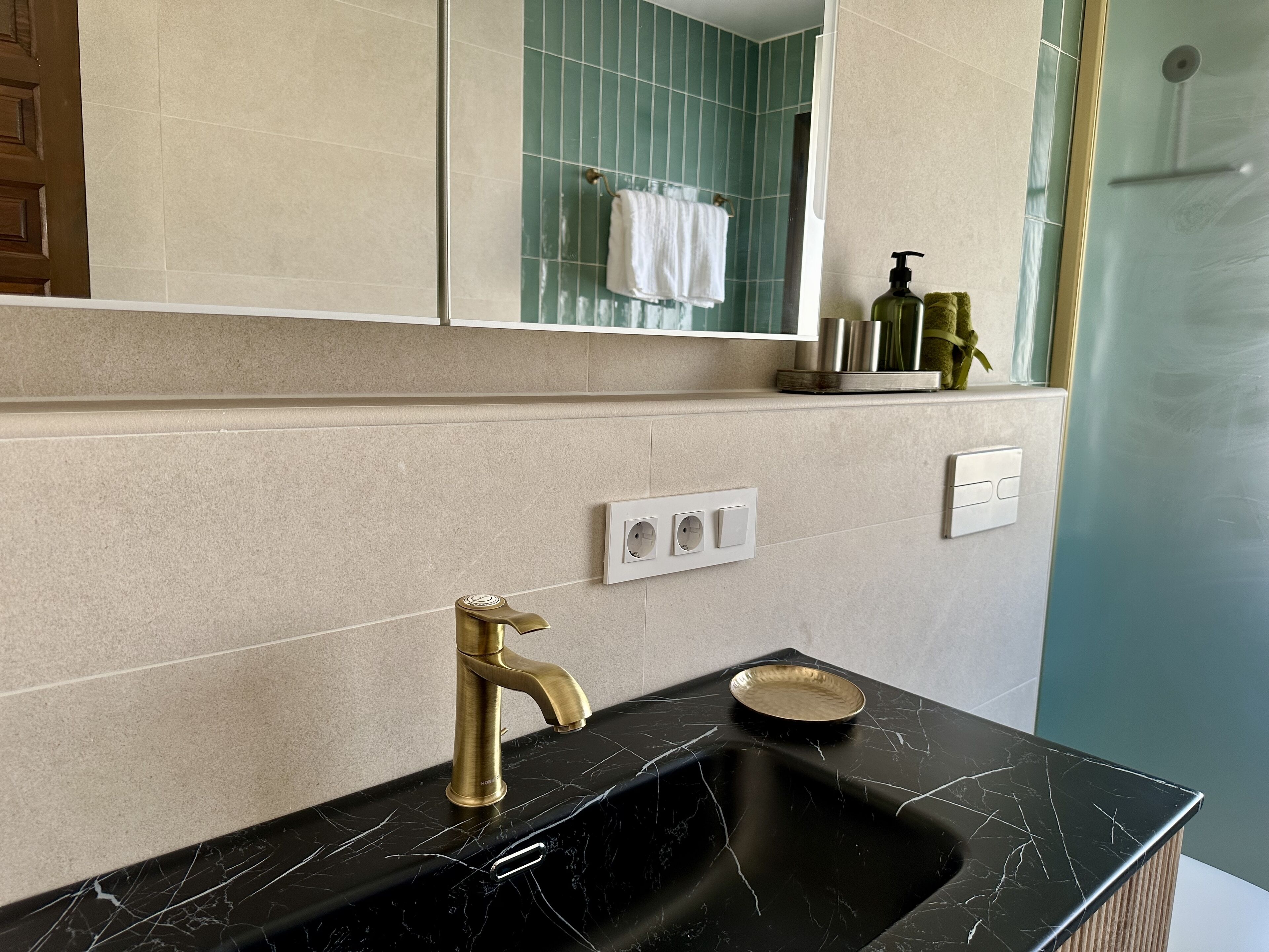 A bathroom with a black marble sink, gold faucet, and a mirror above.