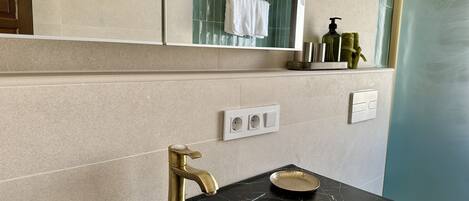 A bathroom with a black marble sink, gold faucet, and a mirror above.