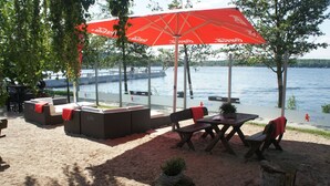 An outdoor seating area with tables and chairs, red umbrellas, and a view of the water. - Large apartment (92 sqm) "sea eagle" 1-6 people in a great location (Kargow)