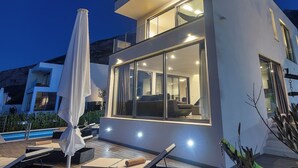 Ein modernes, zweistöckiges Gebäude mit großen Fenstern, Außenbereich mit Sitzgelegenheiten und einem Pool.