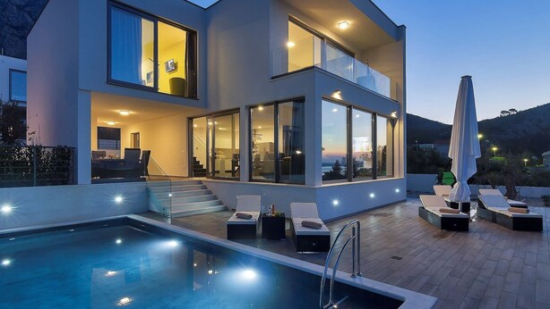 Ein modernes, zweistöckiges Haus mit Pool, Sitzgelegenheiten im Freien und großen Fenstern.