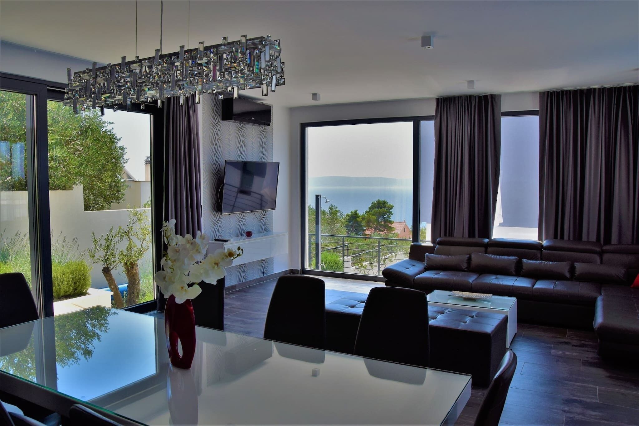 Una sala de estar moderna con un sofá grande, una mesa de comedor con sillas y un televisor montado en la pared.