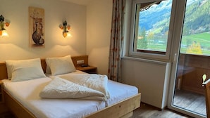 A bedroom with a wooden bed, two bedside tables, a nightstand, and a window with a view of a mountainous landscape.