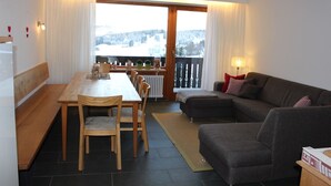 A living room with a dining area, a sofa, and a view of a snowy landscape through a large window.