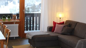 A cozy living room with a sofa, a table, and chairs. There is a view of a snowy landscape through a window.