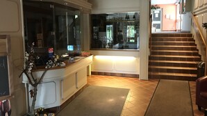 A hotel lobby with a reception desk, a staircase, and a view of the outdoor area.