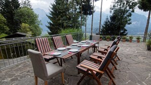 Eine Terrasse mit Tisch für vier Personen, umgeben von Stühlen mit gestreifter Polsterung, mit Blick auf eine gebirgige Landschaft.