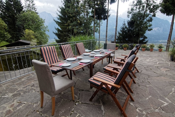 A terrace with a table set for four, surrounded by chairs with striped cushions, overlooking a mountainous landscape. - Ground floor apartment HIGHSPEED W-LAN, 5 persons, terrace/garden for single use (Göriach)
