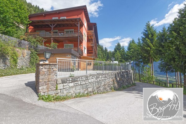 Un edificio de varios pisos con balcones, un muro de piedra y vistas del paisaje circundante.