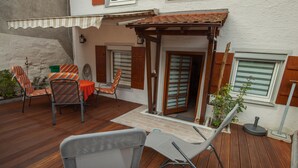 Une terrasse en bois, aménagée avec du mobilier d’extérieur, notamment des chaises et une table, et un espace abrité agrémenté d’une pergola.