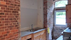 A kitchen with a brick wall, wooden cabinets, a stainless steel sink, and a window with a view of greenery. - Apartment Beta, haven with sauna in an upscale ambience (Weenzen)