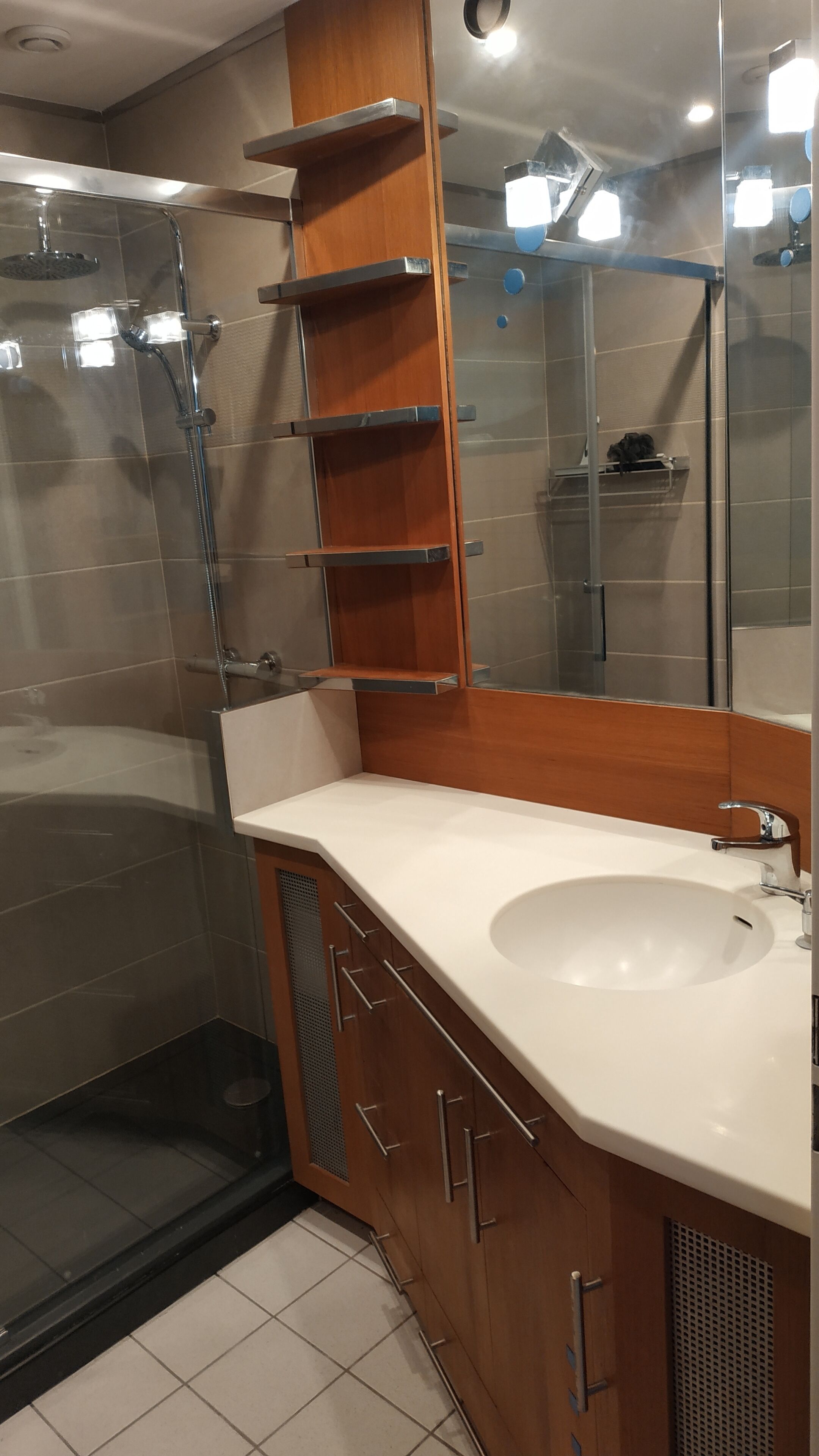 Une salle de bain moderne avec une douche à parois de verre, un meuble-lavabo en bois avec un lavabo blanc et un grand miroir.