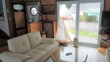 Een woonkamer met een beige bank, een salontafel met glazen blad, een televisie en een model zeilboot.