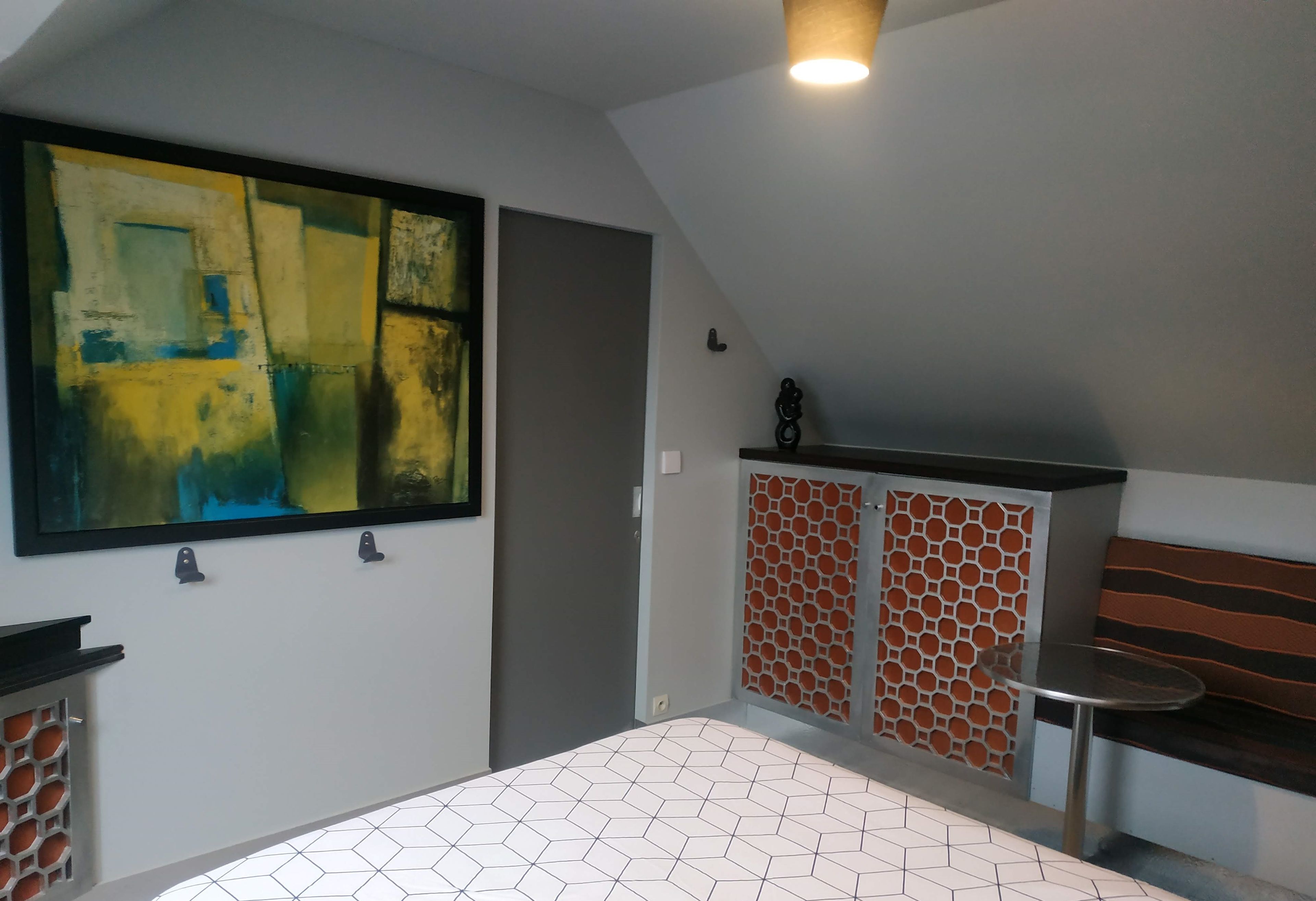 Une pièce moderne avec un sol à motifs géométriques, une grande peinture abstraite et un meuble encastré doté d’une porte à motifs.