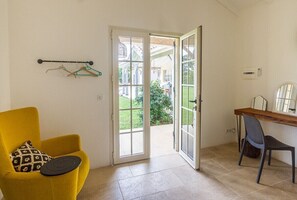 Une pièce avec une chaise jaune, une table avec une chaise, et une porte-fenêtre coulissante donnant sur un jardin.