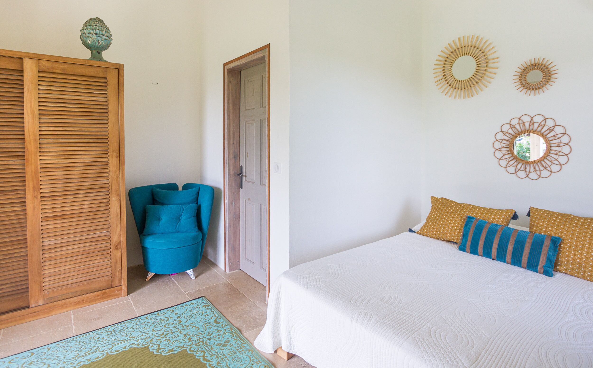 Une chambre à coucher avec un lit, une chaise bleue, une armoire en bois et des œuvres d’art décoratives au mur.
