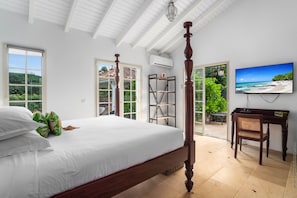 Ein Schlafzimmer mit einem Himmelbett, einem Fernseher, einem Schreibtisch und Blick auf einen Strand durch das Fenster.