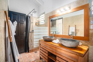 Ein Badezimmer mit einem Holzkosmetikschrank, zwei steinernen Waschbecken, einem großen Spiegel und einer Duschkabine.