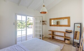 Un dormitorio con una cama, un estante de madera, un espejo y un ventanal corredero que da a un espacio exterior.