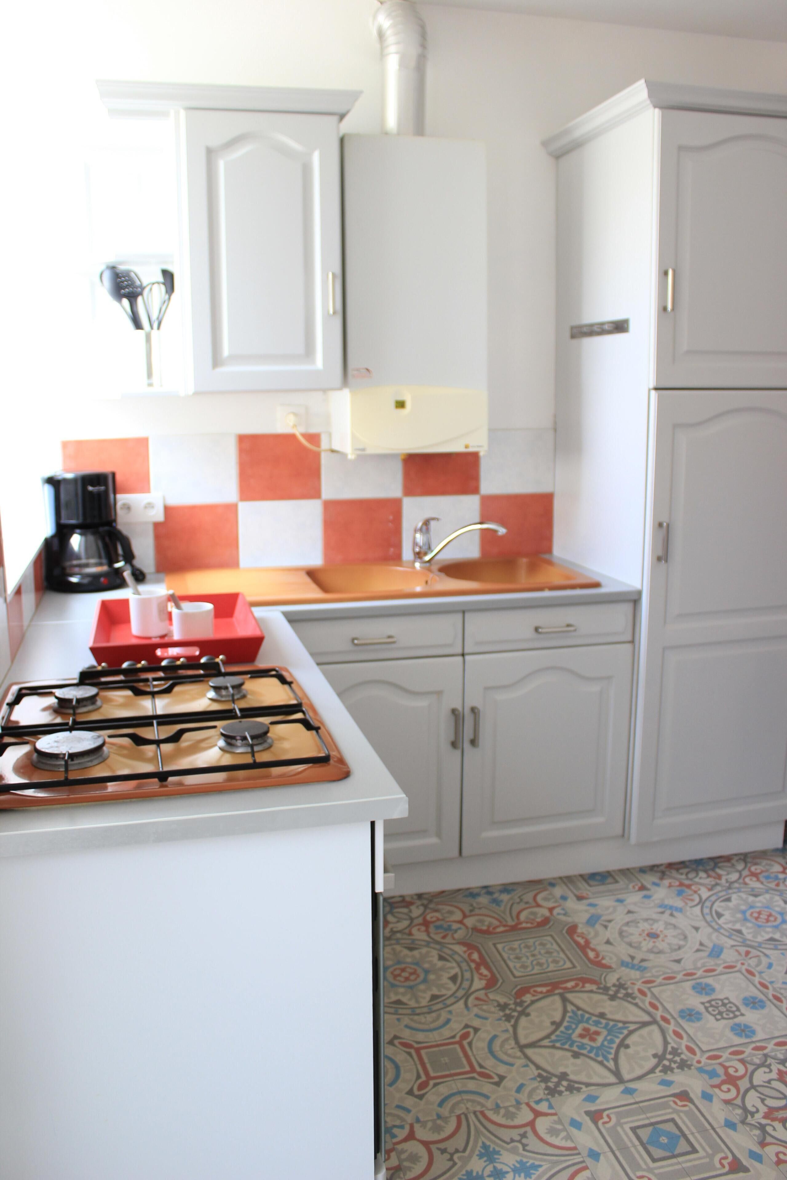 Una cucina con mobili bianchi, piano cottura a gas, lavello e pavimento decorato.