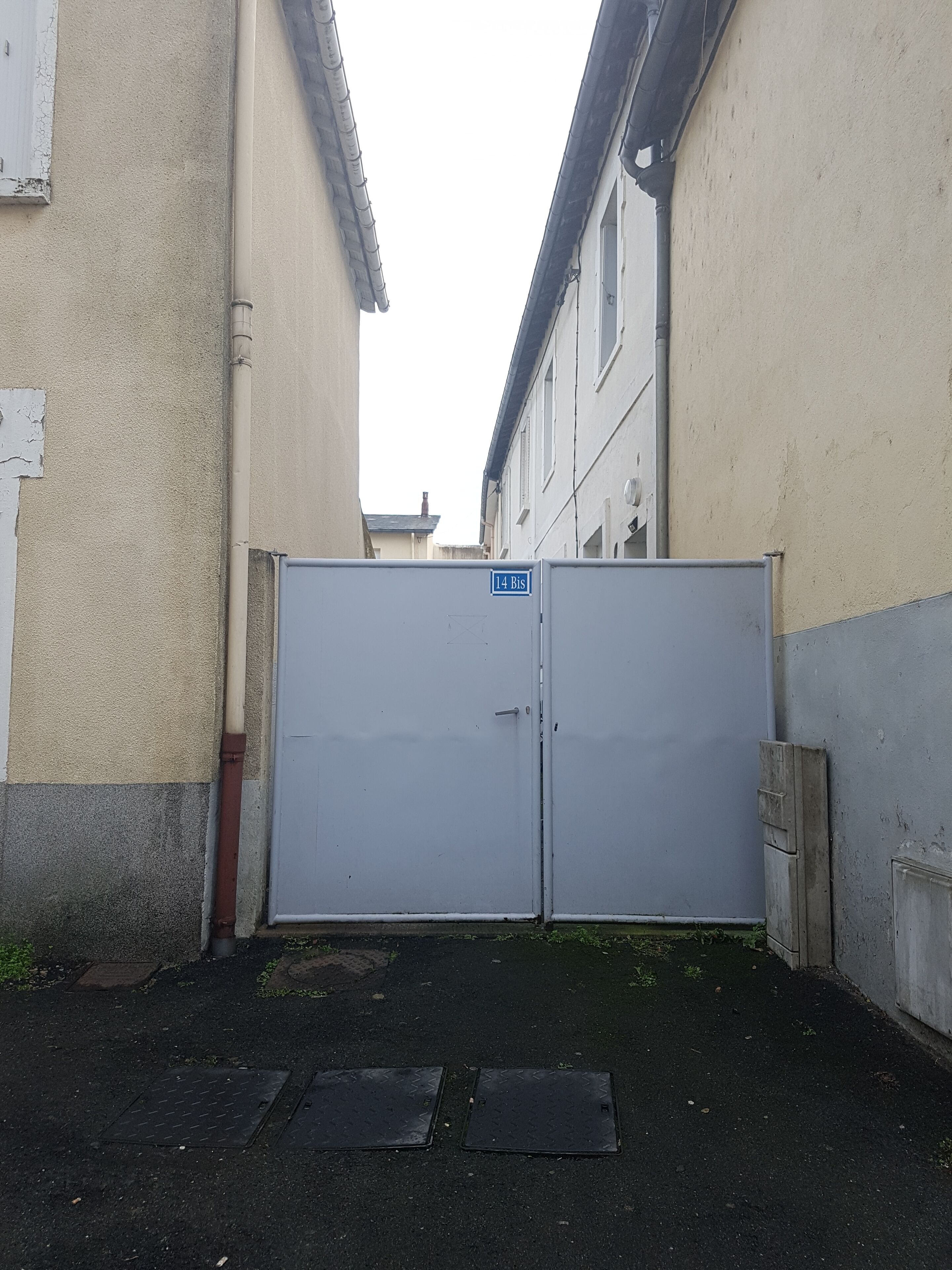 Uma passagem fechada por um portão de metal, paredes de concreto e uma porta de metal com uma placa indicando "14 Bis".