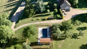 Vista aérea de un castillo con una torre alta, rodeado de jardines cuidados y una piscina.