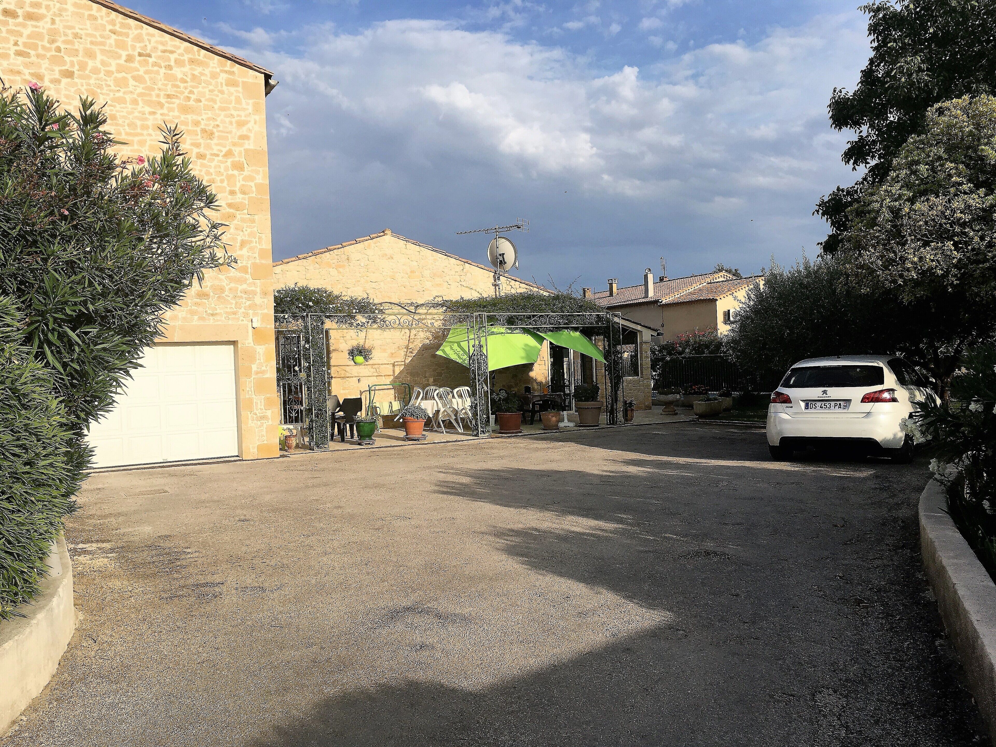 A residential street with a parked white car, a house with a garage, and a patio area with outdoor furniture.