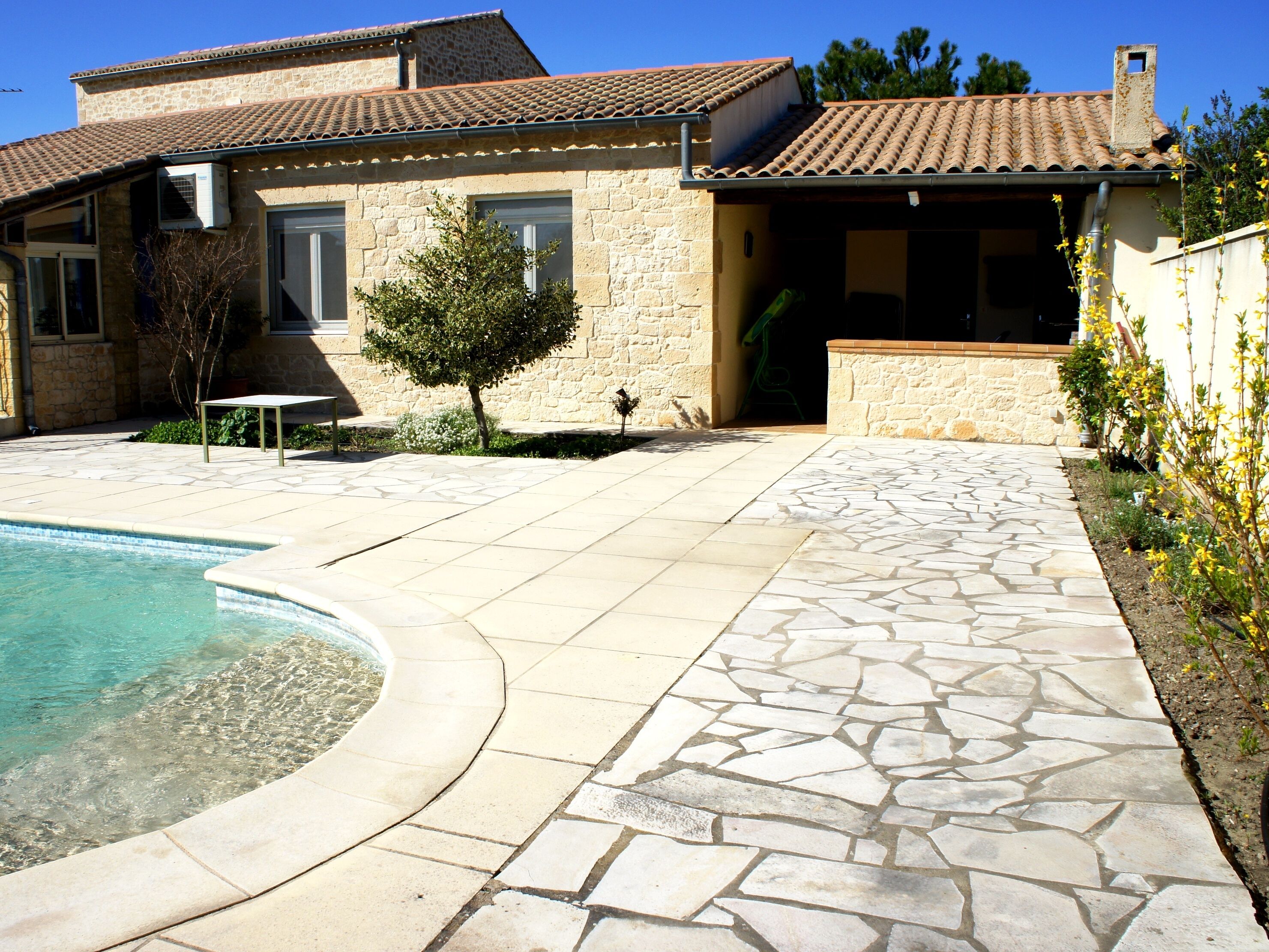 A stone house with a swimming pool, a patio, and a small tree.