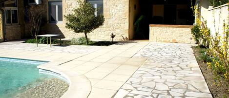 A stone house with a swimming pool, a patio, and a small tree.