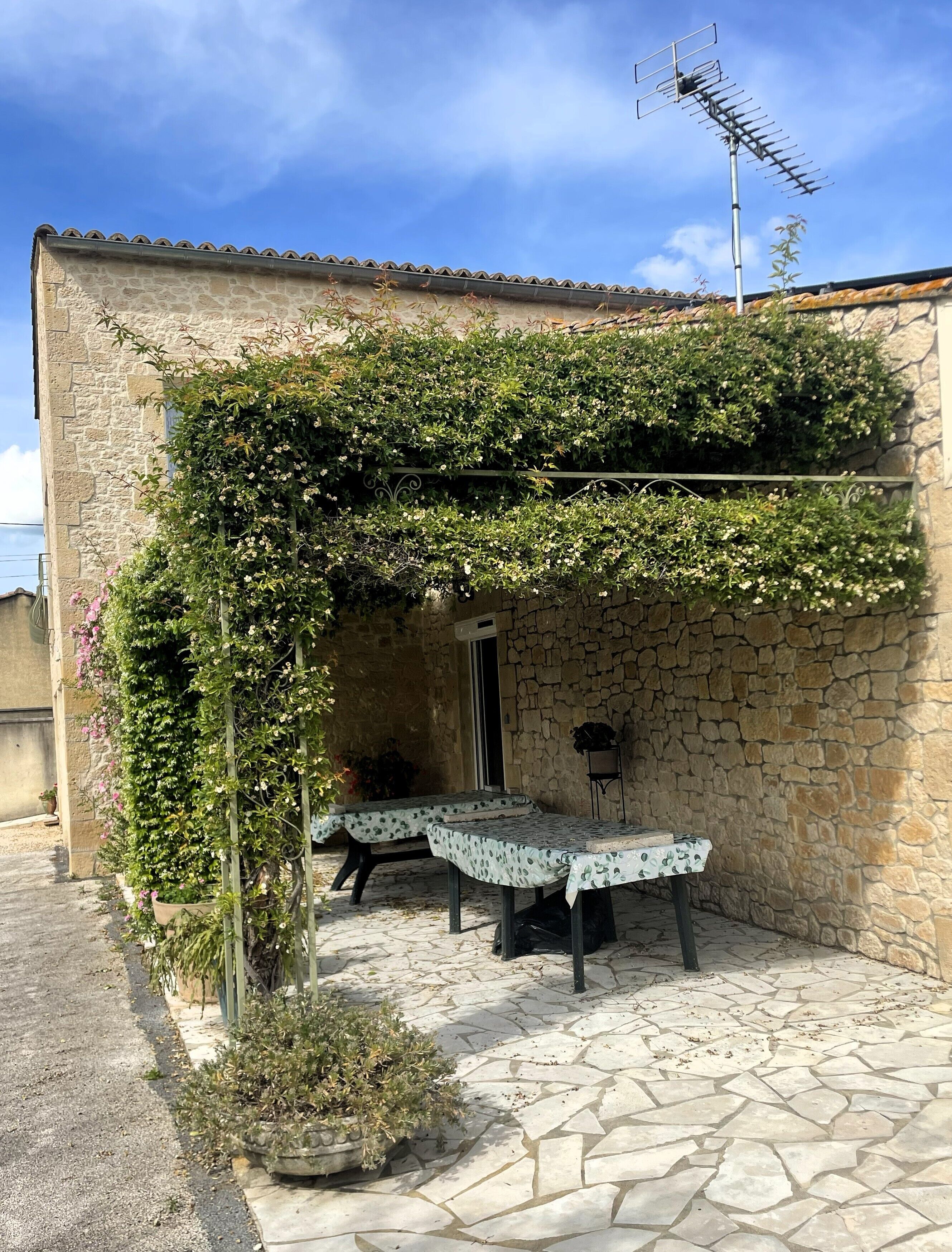 Un bâtiment en pierre doté d’un espace extérieur abrité avec des sièges, une table recouverte d’une nappe à motifs et une antenne sur le toit.