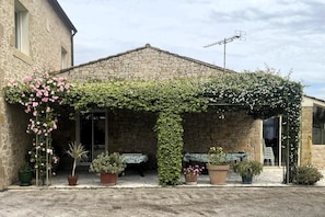 A stone building with a covered patio area, potted plants, and outdoor seating.