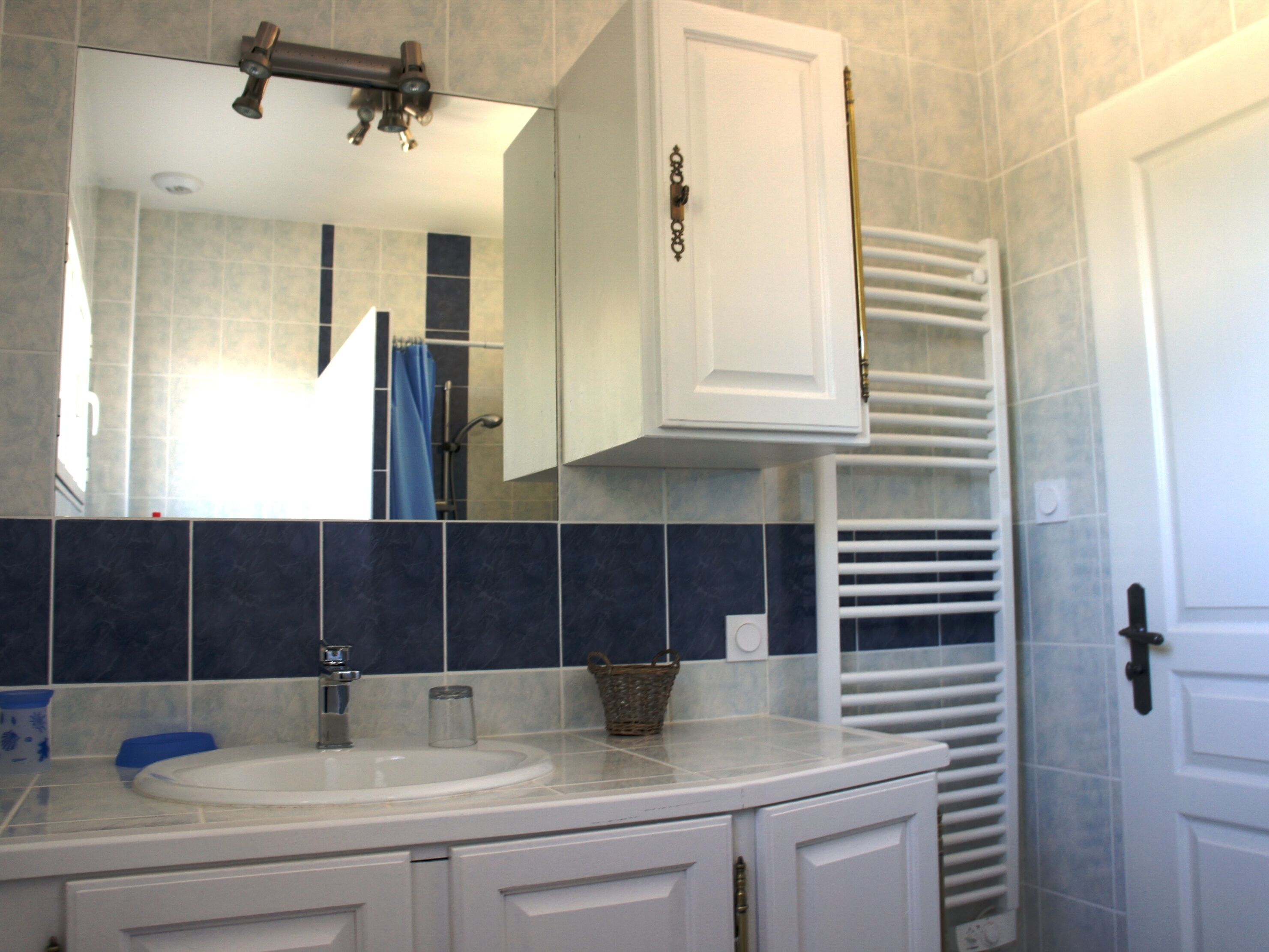 Une salle de bain avec un lavabo blanc, un miroir, un porte-serviettes et une porte.