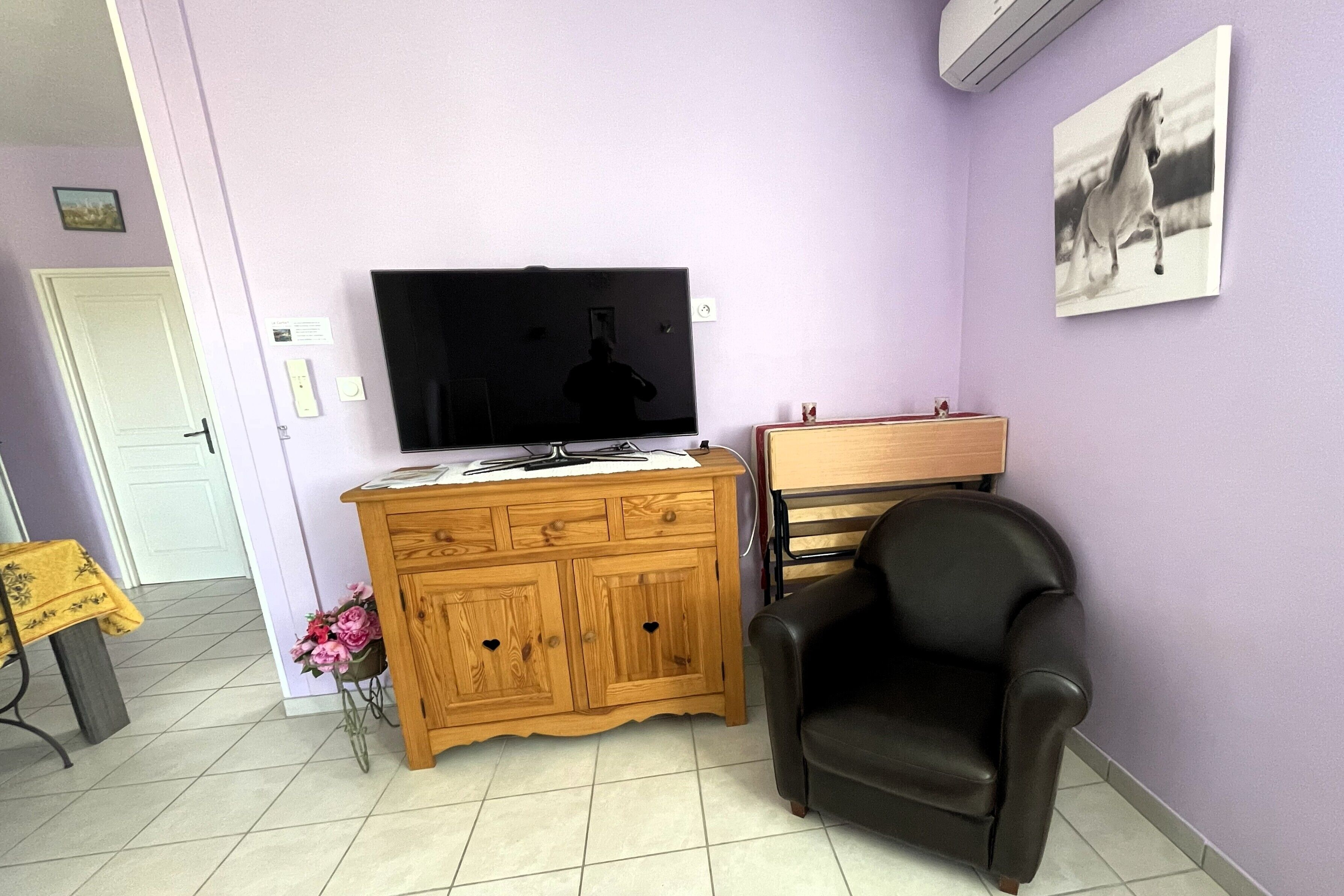A living room with a TV, wooden cabinet, black leather chair, and a painting on the wall.