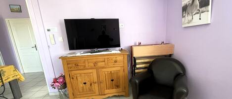 A living room with a TV, wooden cabinet, black leather chair, and a painting on the wall.