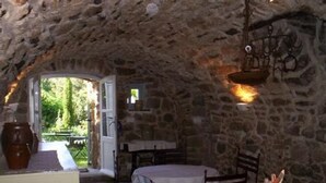 A rustic stone interior with a table and chairs, a hanging light fixture, and a view of greenery outside. - Large independent apartment in a relaxing atmosphere overlooking the sea (Santa-Reparata-Di-Balagna)
