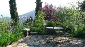 A stone patio with outdoor furniture, surrounded by lush greenery and flowering plants. - Large independent apartment in a relaxing atmosphere overlooking the sea (Santa-Reparata-Di-Balagna)
