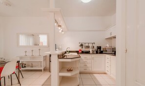 Une cuisine moderne avec des meubles blancs, un coin repas doté d’une table et de chaises blanches, et un petit îlot central avec un évier.