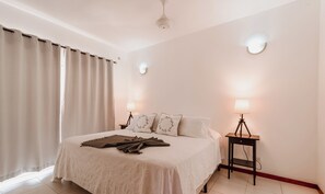 Un lit bien fait, recouvert d’une couvre-lit blanche et agrémenté de coussins décoratifs, deux lampes de chevet et une petite table avec une lampe.