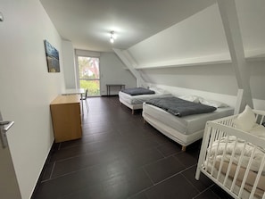 Een moderne, goed verlichte kamer met een schuine kap, een bureau, twee bedden en een wieg.