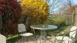 A patio with a round table and four chairs, surrounded by greenery and a yellow flowering tree. - STUDIO GETTE HASPARREN in the Basque Country near the Cambo thermal baths (Hasparren)