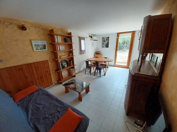 A living room with a sofa, a coffee table, a bookshelf, a dining table with chairs, and a large cabinet.
