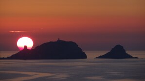 Ein Sonnenuntergang über einem ruhigen Meer, mit zwei markanten Felsen, die sich vor dem Himmel abzeichnen.
