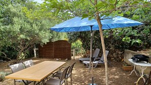 Eine Terrasse mit einem Holztisch und Stühlen, einem blauen Sonnenschirm und einem Grill.