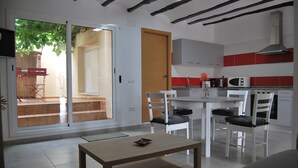 Cocina moderna con armarios blancos, microondas y salpicadero rojo. Hay un comedor con mesa y sillas blancas.