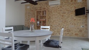 Un comedor con una mesa redonda, sillas blancas, un florero con flores, una pared de piedra y un televisor montado.