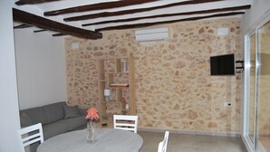 Un comedor con una mesa redonda, sillas blancas, un banco acolchado gris y una estantería de madera, además de una pared con estampado de piedra.