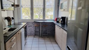A kitchen with a stone backsplash, two stools, a coffee maker, and a window with a view of trees.