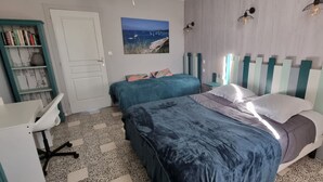A bedroom with two beds, a desk, a bookshelf, and a painting.